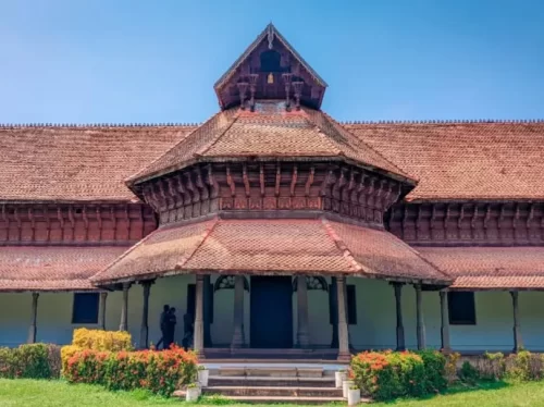 Kuthiramalika Palace Thiruvananthapuram Kerala grand entrance with intricate wooden carvings, sloping terracotta roofs and manicured lawn under vibrant blue sky, perfect India tour package.
