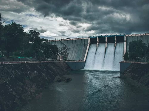 Neyyar Dam majestic concrete gravity structure with cascading white water flows amid lush green trees under dramatic monsoon storm clouds at Neyyar Wildlife Sanctuary Kerala, perfect India tour package.