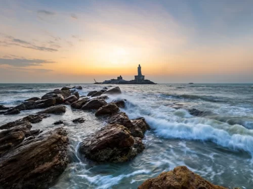 Triveni Sangam at Kanyakumari Beach during sunset, featuring Vivekananda Rock lighthouse and crashing waves, perfect Kanyakumari tour package.