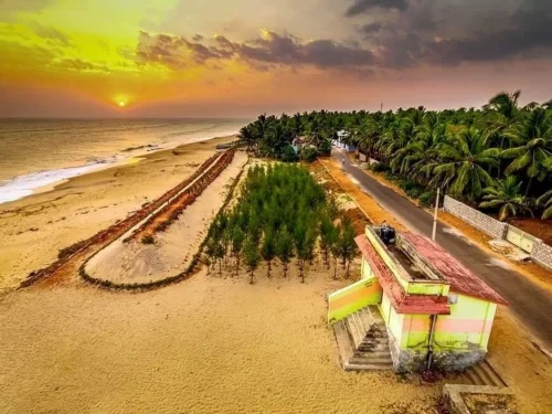 Sunset aerial view of Sanguthurai Beach Kanyakumari with pastel beachside pavilion, neat tree-lined sand barrier, golden shoreline and palm-fringed coastal road, ideal for peaceful Tamil Nadu beach holiday blogs