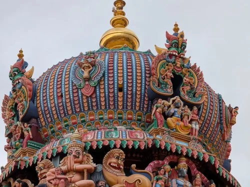 Close-up of Ashtanga Vimana top Arulmigu Koodal Azhagar Temple Madurai Tamil Nadu with multicolored stucco figures deities mythical creatures golden stupika striped roof lion motifs overcast sky, stunning Dravidian temple sculpture detail