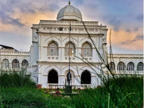 Gandhi Memorial Museum Madurai Tamil Nadu elegant white domed colonial building framed by tall grass foreground Gandhi statue flagpole gardens under golden hour sky, historic freedom tour package