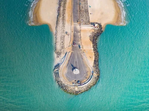 Arichal Munai Beach Dhanushkodi: Drone top-down Pamban road roundabout sandbar turquoise seas rock walls vehicles; India's lands end Ram Setu view.