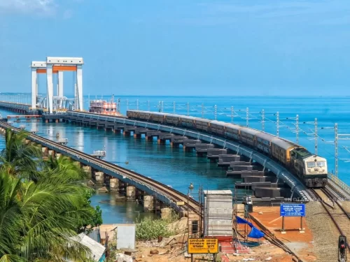 Train crossing new Pamban Bridge in Rameswaram under clear sky, featuring sea channel, pillars, perfect adventure Rameswaram tour package. 