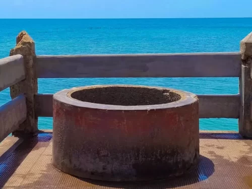 Freshwater well at Villoondi Theertham beach in Rameswaram during sunny day, featuring turquoise sea, rocky railing, perfect spiritual Rameswaram tour package. 