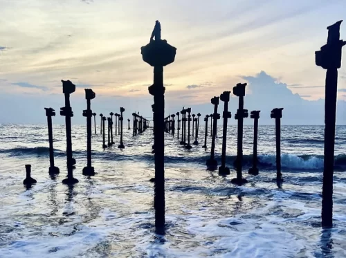 Kerala Kozhikode Beach pier silhouette human figure sunset waves, iconic pillars ocean horizon cloudy skies, perfect Malabar Coast romantic Kerala beach package.
