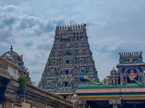 Kapaleeshwarar Temple gopurams in Mylapore Chennai during partly cloudy day, featuring vibrant sculptures, peacocks, Devi idol, lush vines, perfect cultural experience Chennai heritage tour package.