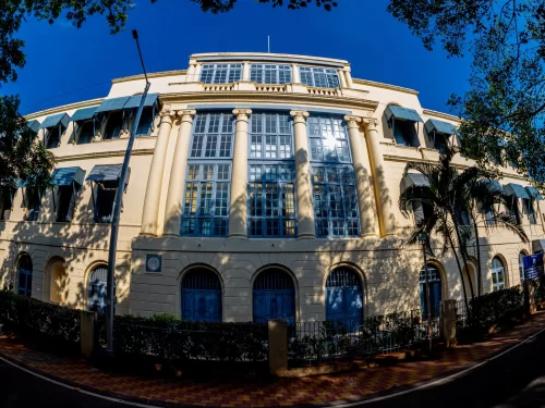Fort St. George Museum Chennai during sunny day, featuring yellow colonial building Corinthian columns verandas palm trees, blue sky shadows, perfect historical heritage Chennai tour package.