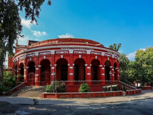 Vibrant circular red-brick Government Museum building with tall arched colonnades, twin stairways, and surrounding greenery under a clear blue sky, highlighting its heritage architecture.