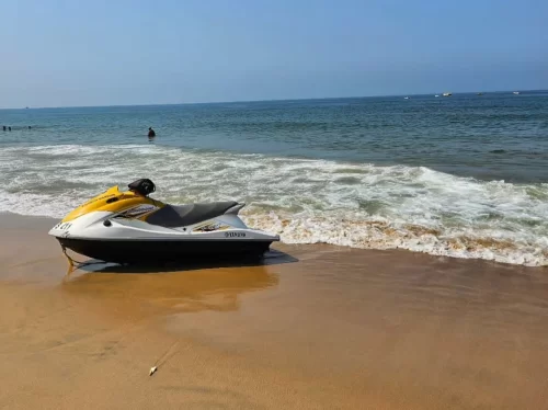 Yellow white jet ski parked on sandy shore at Candolim Beach Goa during sunny day, featuring gentle Arabian Sea waves distant swimmers boats horizon, perfect water sports adventure experience with Candolim Beach Goa tour package.