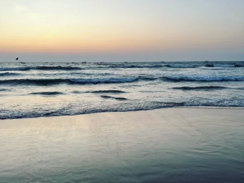 Sunset view of crashing waves at Candolim Beach Goa during golden hour evening, featuring orange sky distant sailboats Arabian Sea horizon, perfect romantic beach experience with Candolim Beach Goa tour package. 