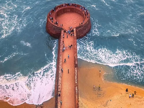 Top-down aerial view of Fort Aguada bastion jetty bastion Sinquerim Beach Candolim Goa with tourists, featuring red laterite circular bastion Arabian Sea waves golden sands, perfect panoramic heritage experience with Fort Aguada Goa tour package. 