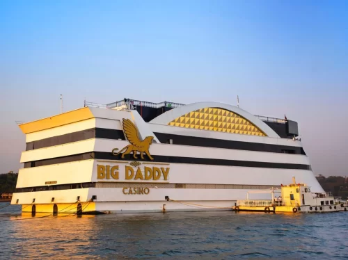 Big Daddy Casino ship on Mandovi River in Goa during sunset, featuring golden lion logo white decks yellow tugboat, perfect gaming adventure experience with Big Daddy Casino Goa tour package