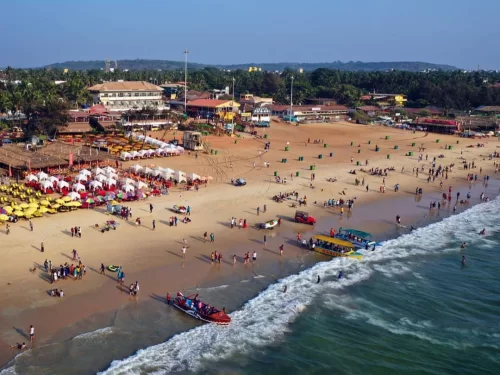 Aerial view of vibrant Calangute Beach Goa during sunny day, featuring colorful umbrellas shack crowds boats Arabian Sea waves, perfect beach adventure experience with Calangute Beach Goa tour package.