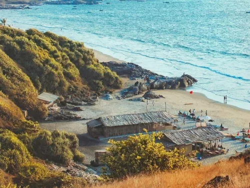 Vibrant Vagator Beach Goa from cliffside with shack beach huts, umbrellas, rocky shoreline and azure Arabian Sea under golden light, perfect boho beach shacks vibe with North Goa tour package. 