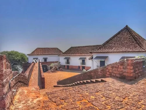 Scenic view of historic Reis Magos Fort Goa with whitewashed buildings red-tiled roofs laterite stone walls ramparts courtyard stairs Mandovi River backdrop clear blue sky, perfect Portuguese colonial heritage photography experience with North Goa tour pa