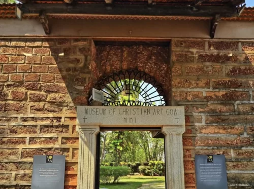 Ornate arched brick entrance gateway to Museum of Christian Art at Convent of Santa Monica Old Goa Goa, featuring wrought iron grille potted plants manicured garden info plaques, perfect heritage experience Old Goa Christian art museum tour package. 