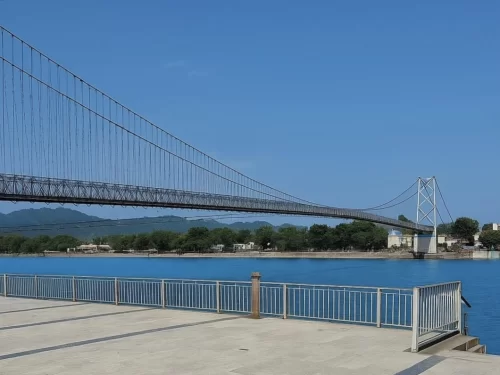 Laxman Jhula suspension bridge at Rishikesh over Ganga River, featuring steel cables towers blue water distant mountains riverside railing, perfect spiritual experience Uttarakhand tour package.