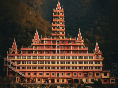 Multi-tiered Trayambakeshwar Temple Rishikesh during twilight, featuring red pagoda-style architecture yellow accents staircases forested hills backdrop, perfect spiritual heritage Uttarakhand tour package.
