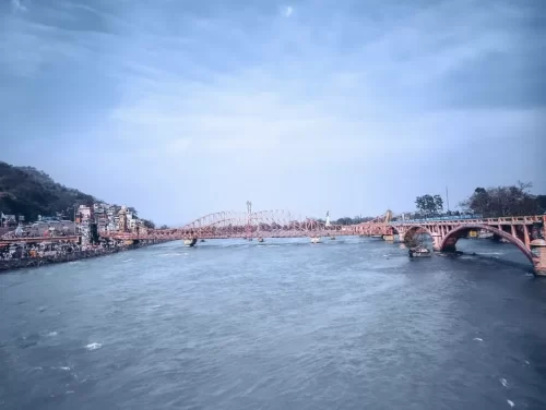 Har Ki Pauri Haridwar iconic pink Lakshman Jhula suspension bridge over Ganga river ghats temples boats cloudy sky hills backdrop, perfect spiritual riverside icon, Uttarakhand tour packages.