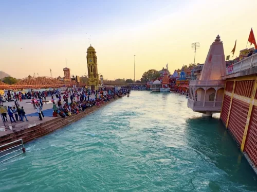 Har Ki Pauri Haridwar golden hour Ganga ghats with yellow clock tower colorful temples tents devotees bridge reflections, perfect spiritual riverside aarti, Uttarakhand tour packages.