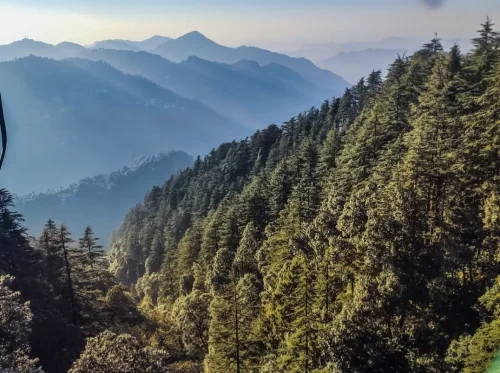 Kempty Falls panoramic sunrise layered misty blue mountains dense green deodar pine forests valley view golden sunlight rays backdrop, perfect scenic viewpoint Mussoorie area Uttarakhand tour packages.