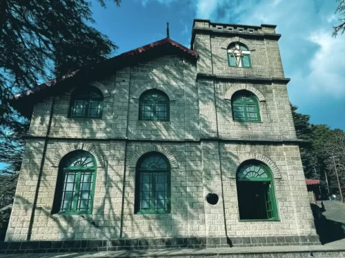 St Paul's Church at Landour during sunny day, featuring colonial stone facade, green windows and deodar trees, perfect romantic Mussoorie tour package.