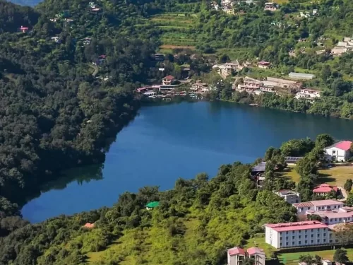 Aerial drone view of Naukuchiatal Lake Nainital during sunny daytime, featuring resorts, village and forested hills, perfect adventure experience Uttarakhand tour package.