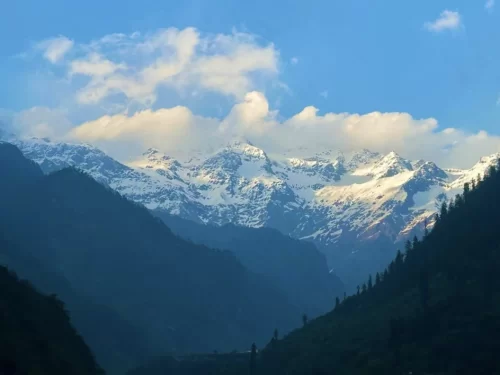 Snow-capped Himalayan peaks at Gangotri valley during clear evening sky, featuring deep green forests, perfect adventure experience Uttarakhand tour package.