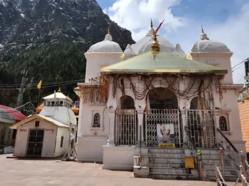 Devotees at Gangotri Temple in Uttarkashi during sunny day, featuring white Nagara-style shrine and Himalayan mountain backdrop, perfect spiritual Uttarakhand tour package.