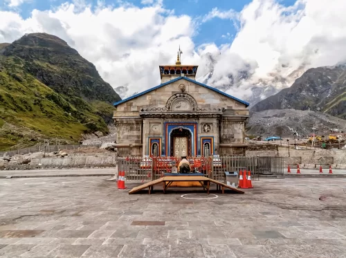 Grand Kedarnath Temple facade at Kedarnath during partly cloudy day, featuring Himalayan peaks saffron barriers ornate doors, perfect spiritual Uttarakhand tour packages.