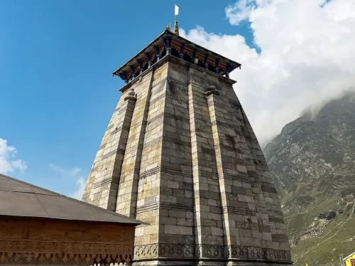 Towering Kedarnath Temple shikharas at Kedarnath during clear daytime, featuring Himalayan peaks saffron flags ornate carvings, perfect spiritual Uttarakhand tour packages.