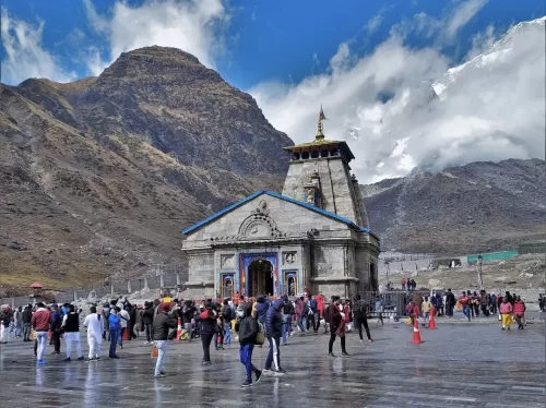 Kedarnath Temple snowy Himalayan peaks crowded pilgrims devotees colorful attire cloudy blue skies stone facade golden kalash, perfect Char Dham Yatra Shiva pilgrimage, Uttarakhand tour packages.