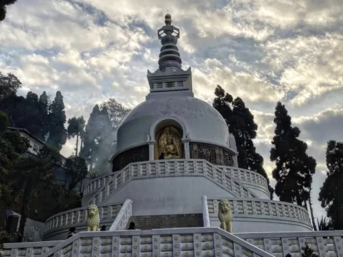 Peace Pagoda Darjeeling during partly cloudy day West Bengal, featuring white stupa golden Buddha statue lion guardians pine hills mist backdrop, perfect West Bengal tour packages.