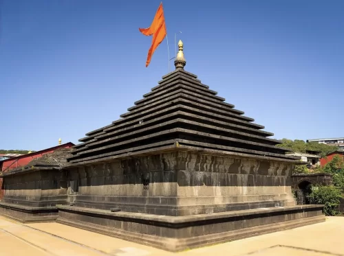 Mahabaleshwar Temple shikhara during sunny day Maharashtra, featuring tiered basalt stone spire saffron flag gold kalash blue sky hill backdrop, perfect Maharashtra tour packages. 