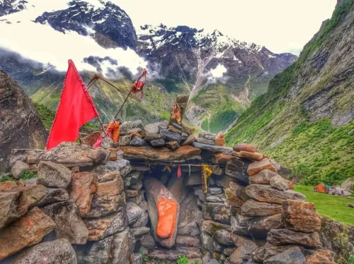 Vishnu Charan Paduka Badrinath stone shrine red flag offerings orange cloth cave snowy Himalayan peaks valley, Uttarakhand Char Dham tour packages. 