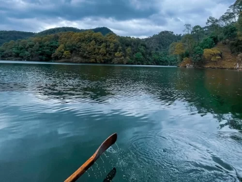 Rowboat paddling at Sattal Lake Nainital during cloudy afternoon, featuring emerald waters and oak-covered hills, perfect adventure experience Uttarakhand tour package.