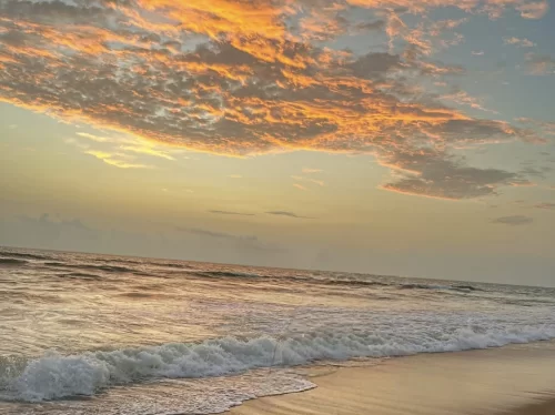 Vibrant sunset at Varsoli Beach in Alibaug, featuring orange clouds, gentle waves and sandy shore, perfect Alibaug tour package