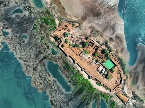 Aerial view of Kolaba Fort near Alibaug, showing its rectangular coastal ramparts surrounded by tidal waters, inner courtyards with temples and greenery, and a distinct green rectangular water tank inside the fort.