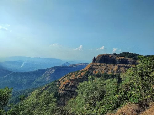 Louisa Point Matheran distant plateau cliffs rocky outcrops green forested valleys hazy blue mountains Western Ghats, perfect Maharashtra hill station expansive viewpoint panorama, Maharashtra tour packages.
