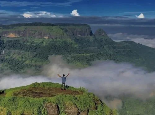 Louisa Point Matheran panoramic viewpoint trek man arms raised green plateau cliffs misty valleys clouds Western Ghats, perfect Maharashtra hill station scenic summit adventure, Maharashtra tour packages.