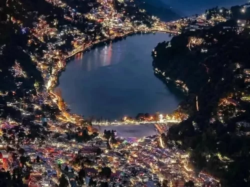 Aerial night view of Naini Lake Nainital, featuring pear-shaped waters reflecting twinkling town lights amid dark hills, perfect romantic experience Uttarakhand tour package.