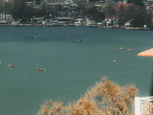 Wide angle boating scene on Naini Lake Nainital during autumn afternoon, featuring multiple rowboats, town shore and distant hills, perfect adventure experience Uttarakhand tour package.