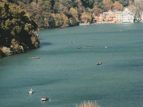 Boating scene on Naini Lake Nainital during autumn afternoon, featuring rowboats, Naina Devi Temple and forested hills, perfect adventure experience Uttarakhand tour package.