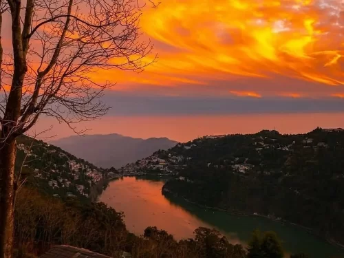 Dramatic orange sunset over Naini Lake Nainital, featuring fiery clouds, pear-shaped waters, town lights and hills, perfect romantic experience Uttarakhand tour package.