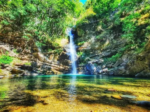 Bhalu Gaad Waterfall near Mukteshwar cascades through lush green forest into turquoise pool, perfect trekking picnic spot, Uttarakhand tour packages.