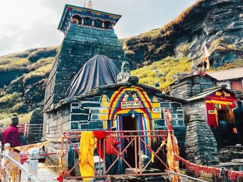 Tungnath Temple facade at hills during cloudy sky, featuring rainbow arch & prayer flags, perfect adventure experience Uttarakhand tour packages. 