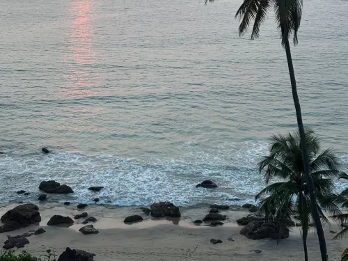 Varca Beach Goa sunset palm silhouettes rocky sands Arabian Sea, pink sun rays calm waves serene horizon, perfect Goa Varca Beach tropical dusk package. 
