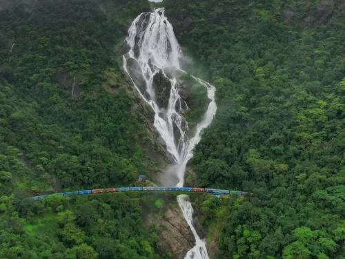 Dudhsagar Waterfall Goa foggy aerial blue train under massive white cascades lush forests, misty Western Ghats hills railway bridge, perfect Goa Dudhsagar Falls train package.