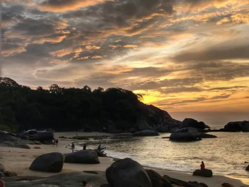 Sunset with silhouettes on Agonda Beach Goa during dramatic sky, featuring boulders fishing boat lush hills, perfect romantic Goa tour package.
